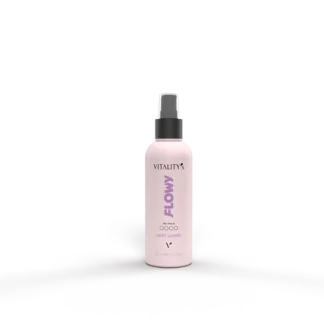 Light pink Vitality Flowy spray bottle with a black nozzle on a pale surface, in front of a pale pink and gray backdrop.