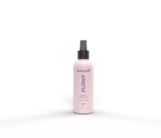 Light pink Vitality Flowy spray bottle with a black nozzle on a pale surface, in front of a pale pink and gray backdrop.